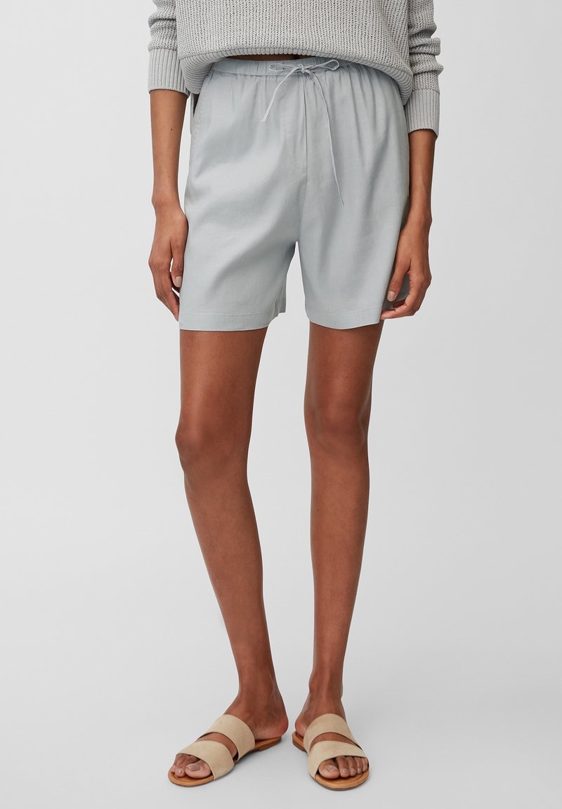Pantalones cortos gris claros con cintura ajustable, que presentan un corte relajado y una textura suave. Combinados con sandalias de playa beige.