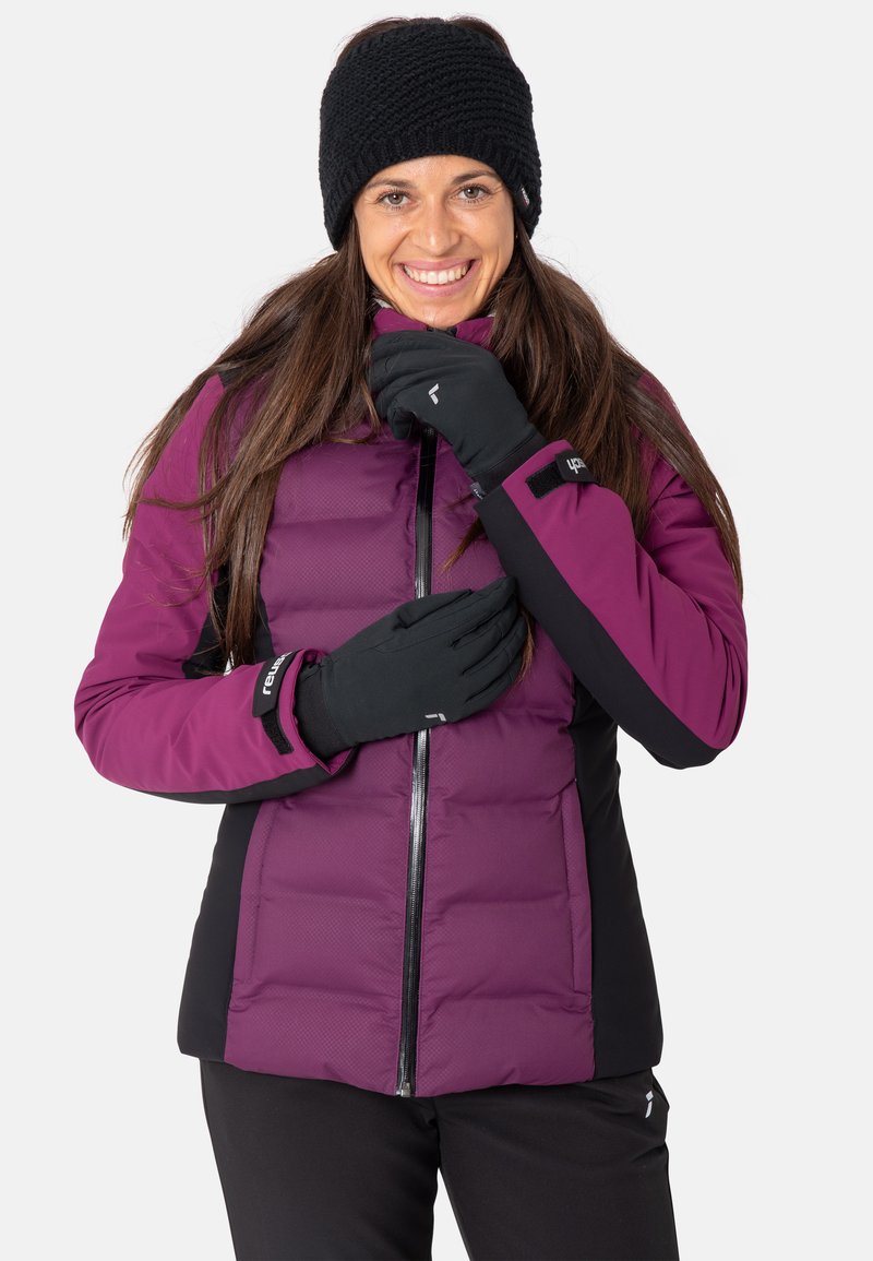 Lila und schwarze isolierte Jacke mit einem Reißverschluss auf der Vorderseite, getragen mit schwarzen Handschuhen. Die Jacke verfügt über ein rautenförmiges Steppmuster und einen hohen Kragen.