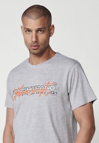 Light gray cotton T-shirt with short sleeves, featuring black and orange graphic text design across the chest. Simple crew neck style.