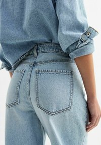 Ljusblå denimjeans med hög midja, traditionella bakfickor och uppvikta fållar. Tyget har en mjuk, texturerad yta.