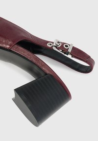 Sandal con tacco in pelle bordeaux, con una fascia testurizzata, accessori in argento e un tacco in gomma spesso. L'interno presenta una finitura liscia nera.