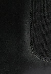 Botín negro con una superficie de cuero liso y un panel elástico texturizado en contraste. Incluye costuras blancas detalladas a lo largo de los bordes.