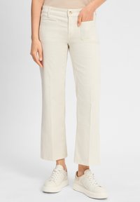 Helle beigen, weit geschnittene Hose aus Baumwolle mit glatter Textur, mit Vorder- und Hintertaschen, kombiniert mit weißen Sneakern.