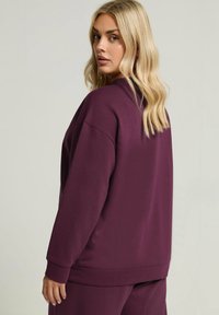 Burgunderfärgad oversized sweatshirt med avslappnad passform, ribbade ärmslut och en mjuk textur, med minimal sömnadsdetaljer och rund halsringning.