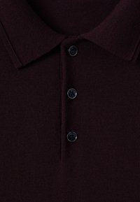 Donkerbruine gebreide poloshirt in close-up met een opgevouwen kraag en drie zwarte knopen langs de knoopsluiting.