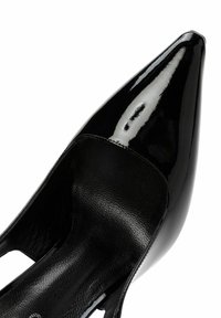 Zapatos de tacón de charol negro con punta afilada y acabado brillante, que cuentan con un diseño de corte lateral y un forro interior texturizado en negro.