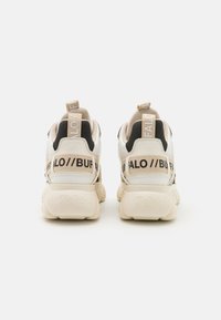 Vita och svarta sneakers med tjocka sulor, utrustade med beige detaljer och varumärkeslogotyper på hälen och baksidan. Strukturerad överdel för stöd.