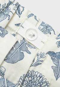 Tissu à imprimé floral avec des motifs botaniques bleus sur fond crème. Présente un band élastique blanc et un détail de bouton transparent.