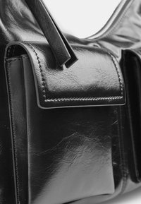 Juodas odinis rankinukas su tekstūruotu paviršiumi, plokščiu priekinio kišeniu ir užtrauktuko uždarymu viršuje. Akcentinės siūlės prideda dizainui detalių.