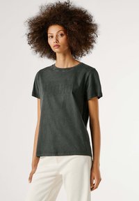 Tume roheline, lühikeste varrukatega T-särk ümarate krae ja lahjate perforeeritud tekstikee detailidega rinnaosas. Sile puuvillane kangas.