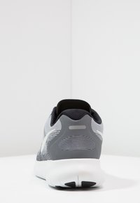 Vista posteriore di una scarpa sportiva grigia e bianca con rivestimento interno nero su una superficie bianca contro uno sfondo bianco uniforme.