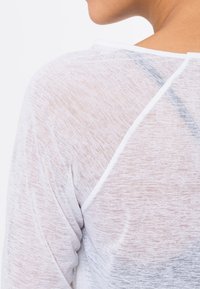 White lightweight top with a sheer, textured fabric. Features a round neckline and raglan sleeves, showcasing a soft, layered appearance.