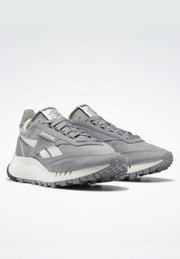 Paire de baskets grises Reebok avec détails en mesh et daim, semelles blanches épaisses et semelles extérieures en caoutchouc gris à motifs, présentées sous un angle.