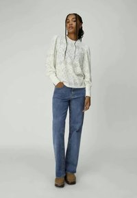 Light beige knitted sweater with intricate cutout pattern, paired with mid-blue straight-leg jeans and brown clogs. Simple, casual design.