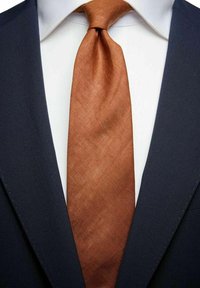 Merihenkinen puku, jonka pinta on sileä, ja sitä täydentää kudottu, ruosteenvärinen solmio. Valkoisen kauluspaidan kaulus näkyy puvun alta.