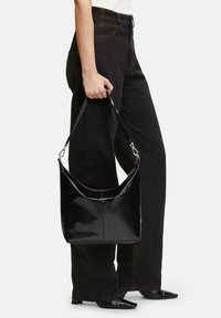 Czarna, lakierowana skórzana torebka na ramię o zaokrąglonym kształcie, z zamkiem błyskawicznym i odpinanym paskiem. Gładka, błyszcząca tekstura z minimalną ilością okuć.