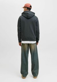 Mørk grå hættebluse, løstsiddende lys grøn denimbukser med falmet farvegradient, båret med beige sko og en pink kasket.