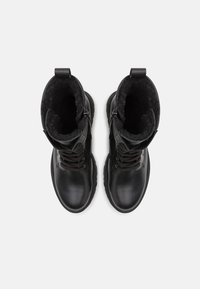 Botas de couro pretas com forro texturizado, bico redondo, fecho com atacadores à frente e fechos laterais; solas de borracha duráveis para aderência e suporte.