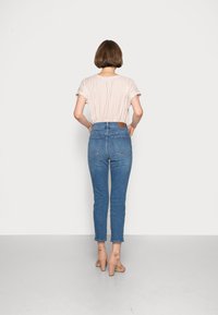 Beige randig t-shirt med kort ärm som bärs med högmidjade blå jeans. Jeanspocketarna är i brunt läder och har två bakfickor. Sandaler med klack.