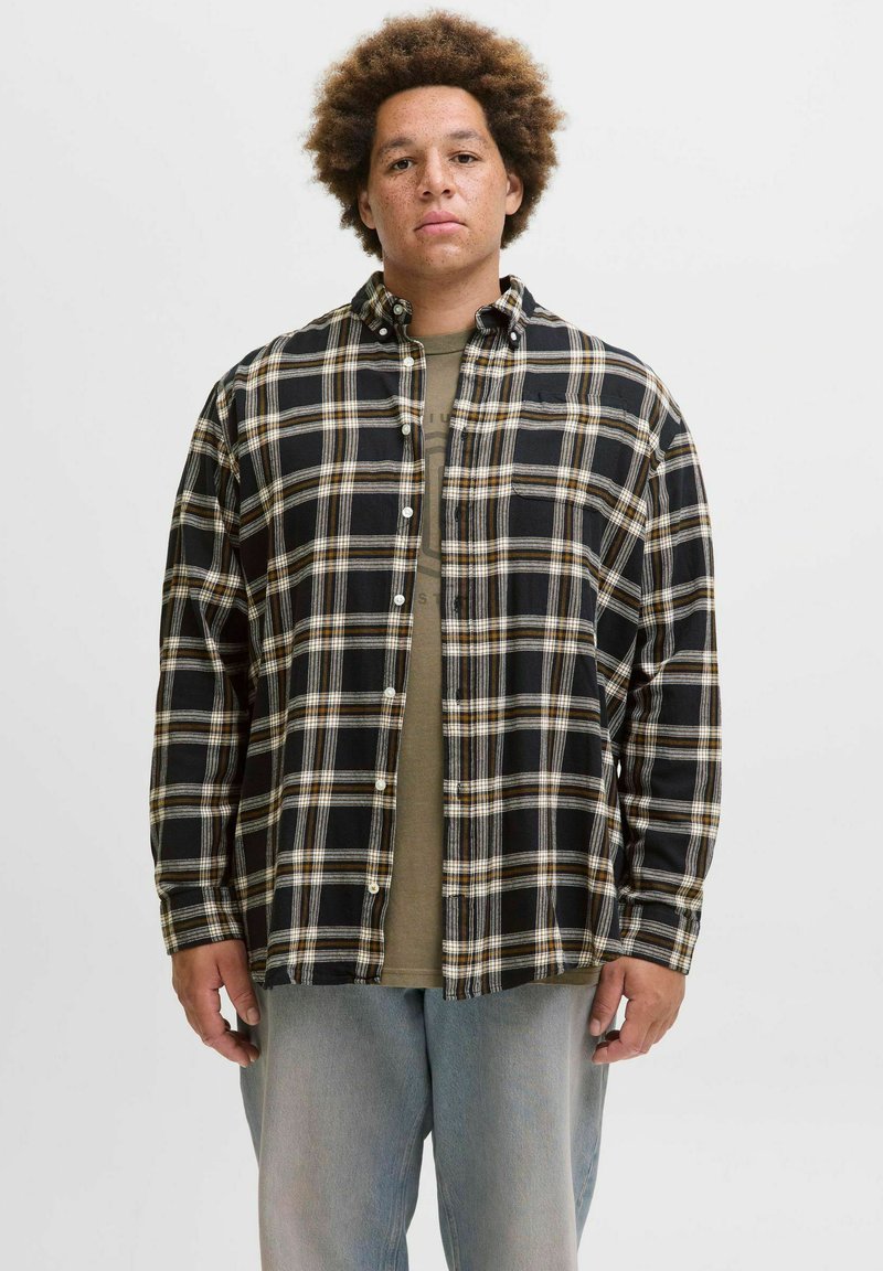 Sort/hvid ternet flannel skjorte med beige detaljer, med knaplukning foran og en afslappet pasform, båret over en olivengrøn skjorte.