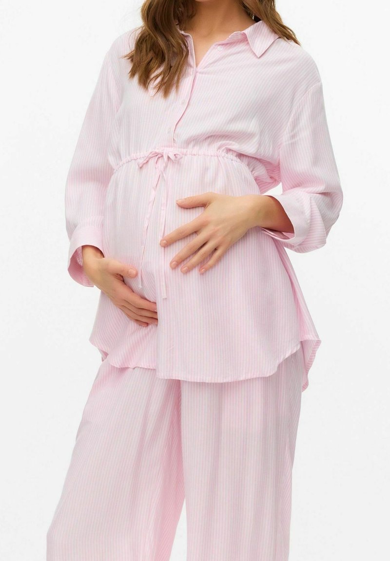 Femme enceinte portant un pyjama ample à rayures rose clair, tenant doucement son ventre avec les deux mains.