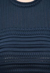 Gros plan sur un tissu en maille bleu marine avec des motifs côtelés verticaux et horizontaux alternés et de petites perforations.