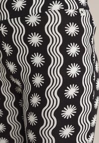 Črna tkanina z ponavljajočim se vzorcem valovitih belih črt in zvezdastih oblik, z teksturirano površino. Poudarjena je z majhnim zvezdastim logotipom.