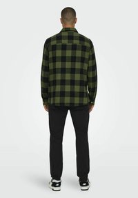 Groene en zwarte geruite flanellen shirt met een kraag met knopen, lange mouwen en een relaxte pasvorm, gecombineerd met zwarte broek en sneakers.