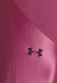 Fuchsiové sportovní tílko s hladkým, elastickým materiálem a kontrastními texturami, na kterém je logo Under Armour v tmavě fialové barvě.