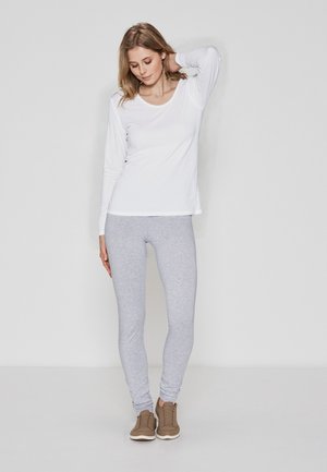 Hvid langærmet top og lysegrå leggings lavet af en bomuldsblanding. Sættet har en afslappet pasform og er parret med brune sneakers.