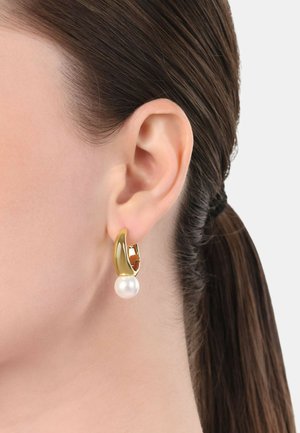 Gouden oorbel met een gebogen ontwerp, voorzien van een gladde witte parel als accent. De oorbel klikt stevig aan het oor voor veilig dragen.