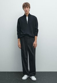 Maglione nero a mezze zip con polsini a costine, abbinato a pantaloni neri a gamba larga e scarpe da ginnastica bianche. Design semplice e minimalista senza motivi.