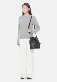 Maglione grigio a maglia, pantaloni bianchi a gamba larga e una borsa a secchiello in pelle nera con finiture dorate e una tasca frontale, dotata di una tracolla rimovibile.