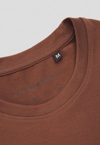 Brązowy bawełniany t-shirt z okrągłym dekoltem, z wyraźną metką marki i ikonami nadrukowanymi wewnątrz kołnierza z instrukcjami pielęgnacji.