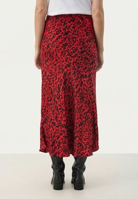 Red leopard-print midi skirt with a flowing design, smooth texture, and a ruffled hem. Worn with tall black boots.