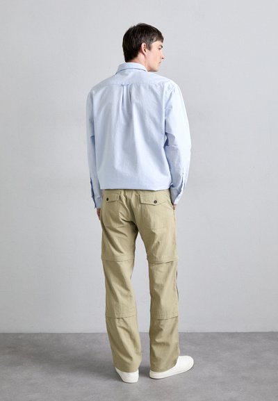 Chemise bleu clair à manches longues avec un dos fendu, associée à un pantalon cargo beige avec des poches et une coupe décontractée. Porté avec des baskets blanches.