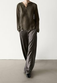 Chemise à manches longues vert olive avec un col boutonné, associée à un pantalon ample en satin gris à la texture lisse.