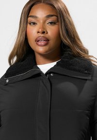 Czarna kurtka puchowa z teksturowanym czarnym kołnierzem z polaru. Posiada zamek błyskawiczny oraz zatrzaski. Wykonana z lekkiego materiału o gładkim wykończeniu.