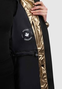 Giacca nera con una fodera interna dorata lucida, caratterizzata da una toppa con logo e dettagli con bottoni. Il tessuto ha una trama liscia.