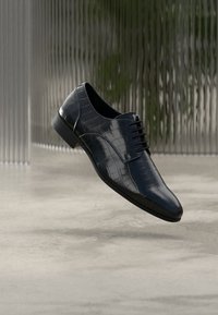 Chaussure en cuir noir à texture crocodile avec un bout pointu et un design à lacets. Présente une finition lisse et une silhouette élégante.