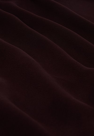 Dunkelburgunderfarbener Stoff mit weicher, glatter Textur, die sanfte Wellen und Falten zeigt, ohne erkennbare Muster oder Verzierungen.