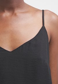 Haut sans manches noir avec un décolleté en V et des bretelles fines, fabriqué à partir d'un tissu lisse et léger avec une texture subtile.