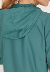 Lichtgewicht, teal kleurige hoodie met een gladde textuur, voorzien van een strakke capuchon en subtiele naden. De achterkant heeft een strak ontwerp zonder versieringen.