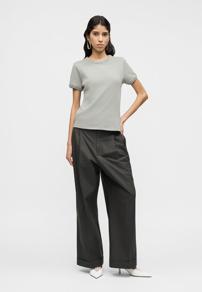 Ανοιχτό γκρι εφαρμοστή μπλούζα με κοντά μανίκια, συνδυασμένη με σκούρο γκρι παντελόνι φαρδιάς γραμμής. Λευκά ψηλοτάκουνες γόβες με μυτερή μύτη. Απλός σχεδιασμός, λείο ύφασμα.