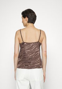 Cami top em cetim castanho com um padrão de riscas de zebra, alças finas e um corte descontraído. Apresenta uma tatuagem gráfica no braço superior.