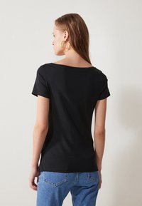 Svart t-skjorte med kort erme og båtutringning, laget av glatt bomullsstoff, kombinert med lyseblå denimjeans. Ingen synlige mønstre.