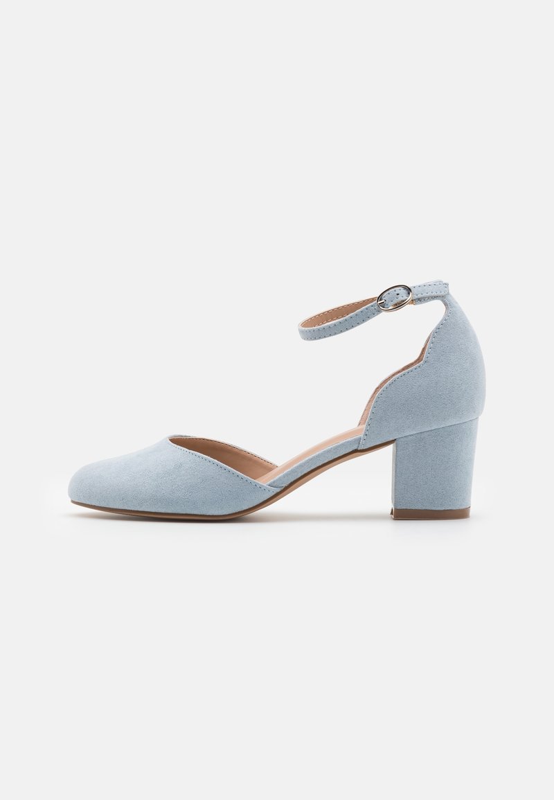 Chaussure en daim bleu clair à bout fermé avec talon bloc et bride à la cheville ornée d'une boucle ronde argentée, vue de profil.