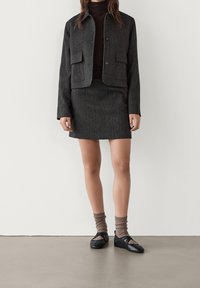 Gray wool-blend jacket with two front pockets, paired with a matching skirt. Black flat shoes and brown ribbed socks complete the outfit.