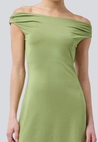 Abito off-the-shoulder in tessuto morbido e stretch, caratterizzato da un delicato colore verde e da una leggera drappeggiatura al collo. Design semplice e aderente.