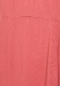 Tecido coral com um acabamento texturizado, apresentando um padrão de pontos subtil. O material é leve e flui suavemente.